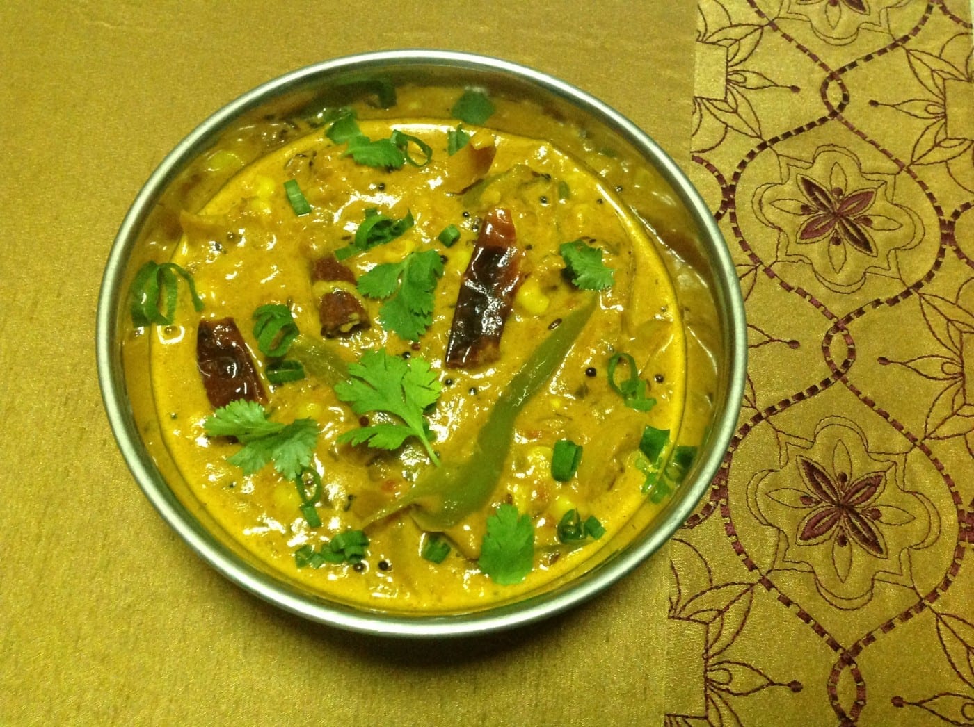Overhead view of a steel bowl filled with bell pepper makhani on a yellow dinner mat