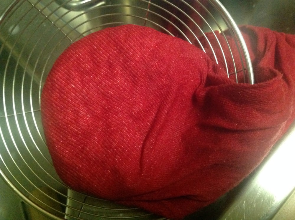 Cheese cloth with paneer sitting on a sieve
