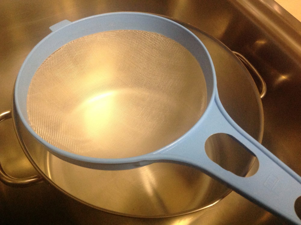 A nylon sieve over a stainless steel pan in a sink 