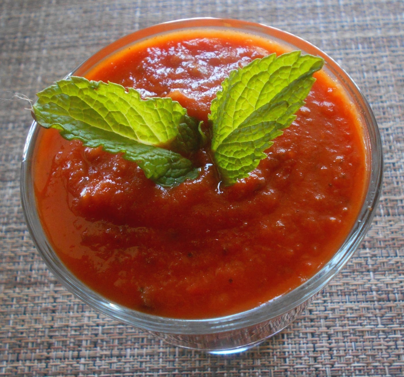 A glass bowl filled with homemade marinara sauce and topped with mint leaves for garnish