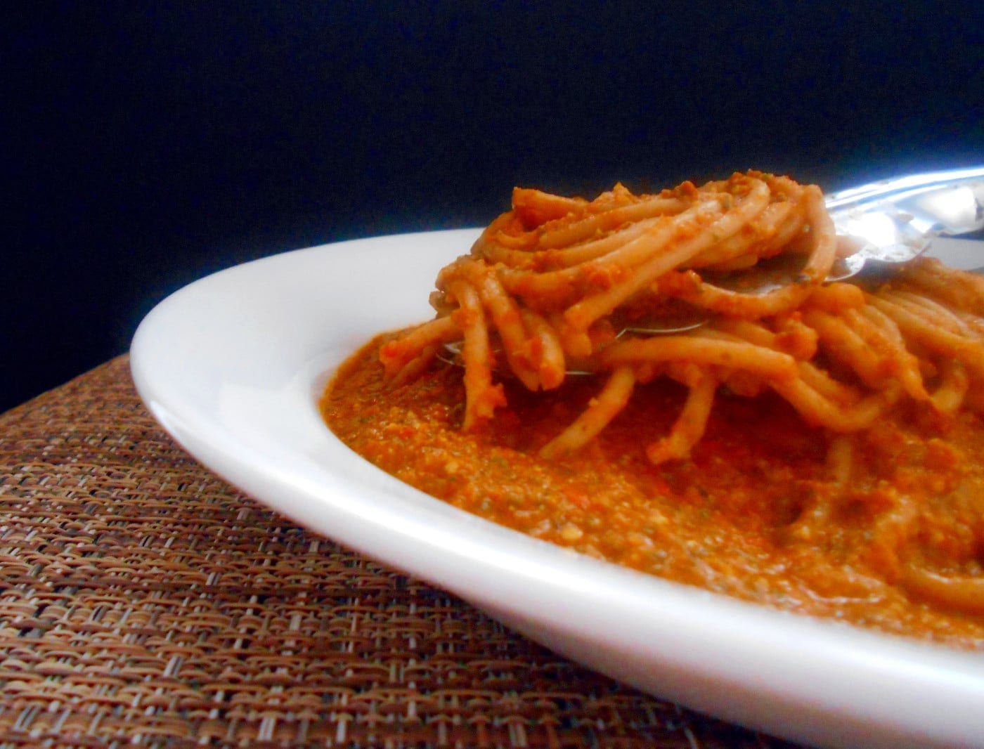 Closeup view of a tongs grabbing spaghetti with tomato pesto on a white dish