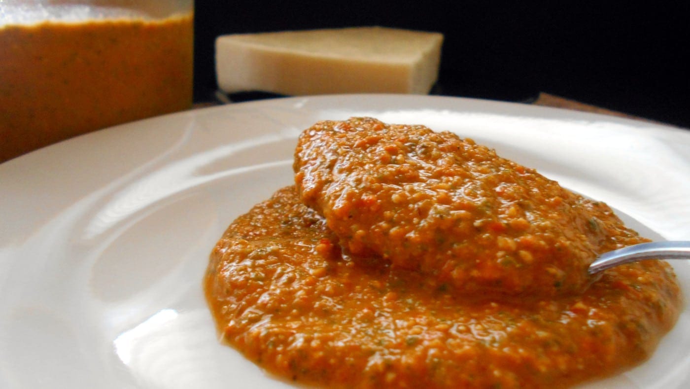 Side view of a spoon filled with tomato pesto on a white dish