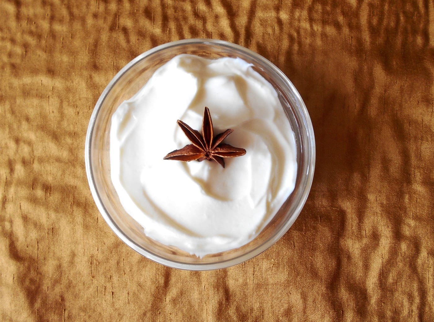 Overhead view of a clear bowl filled with yogurt dressing and topped with a star anise