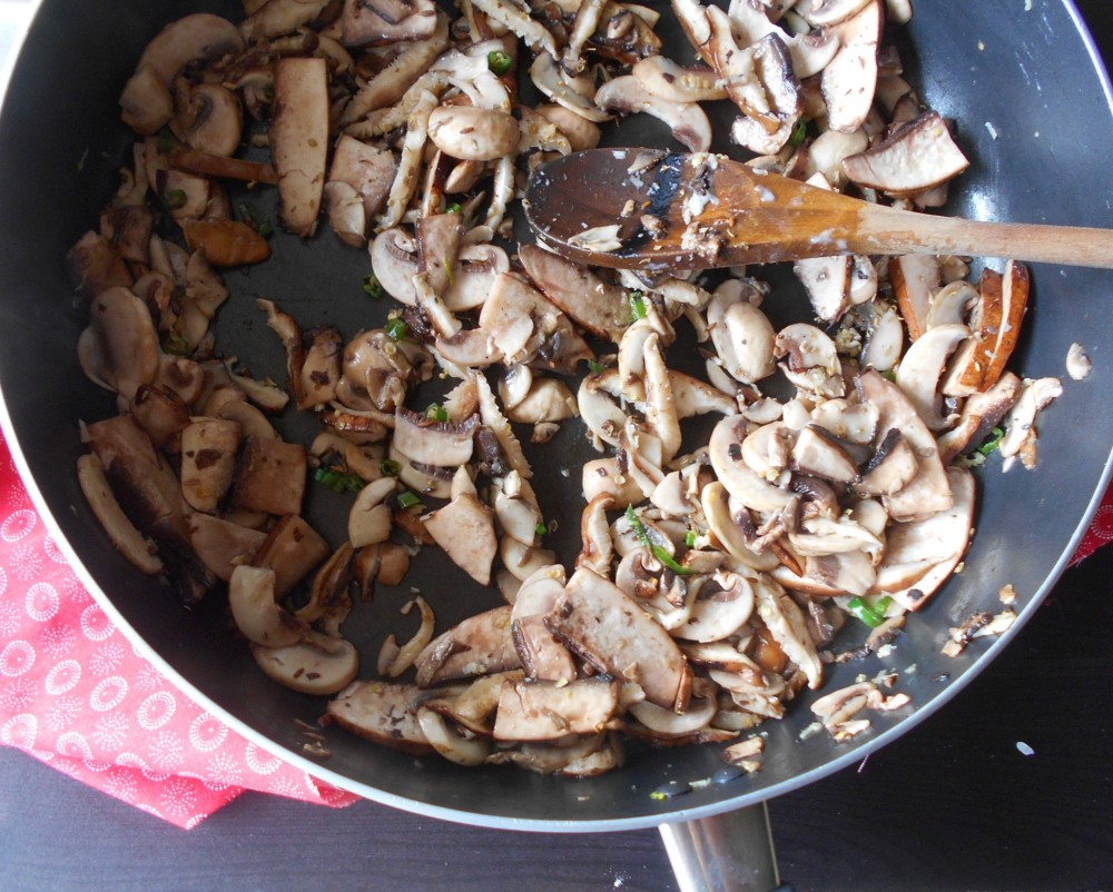 Overhead shot of mushrooms iin a cast iron skillet with a wooden stirring spoon on the side