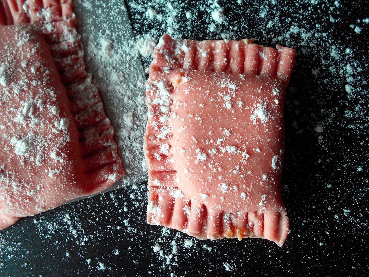 Overhead view of a single tomato ravioli lightly floured. On the side, part of another ravioli is visible