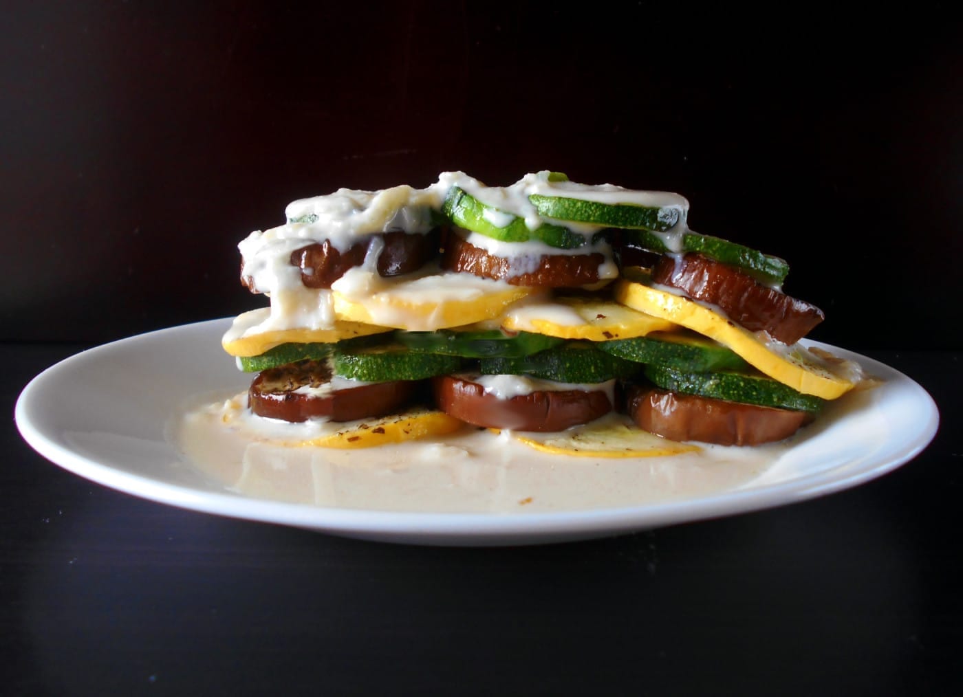 Front view of a stack of fresh veggies doused with soubise sauce - Ratatouille Stack