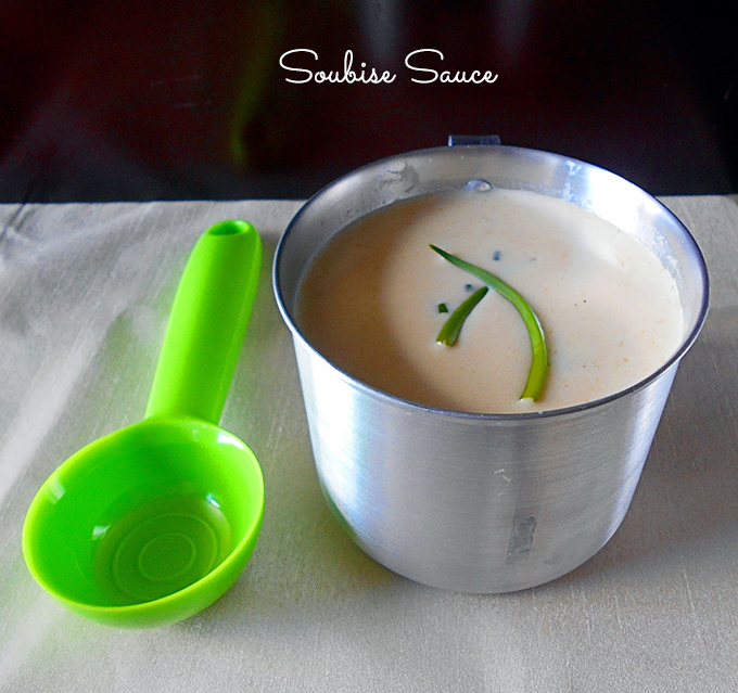 Front View of a Steel Measuring Cup Filled With Soubise Sauce and a Green Plastic Spoon Next to it