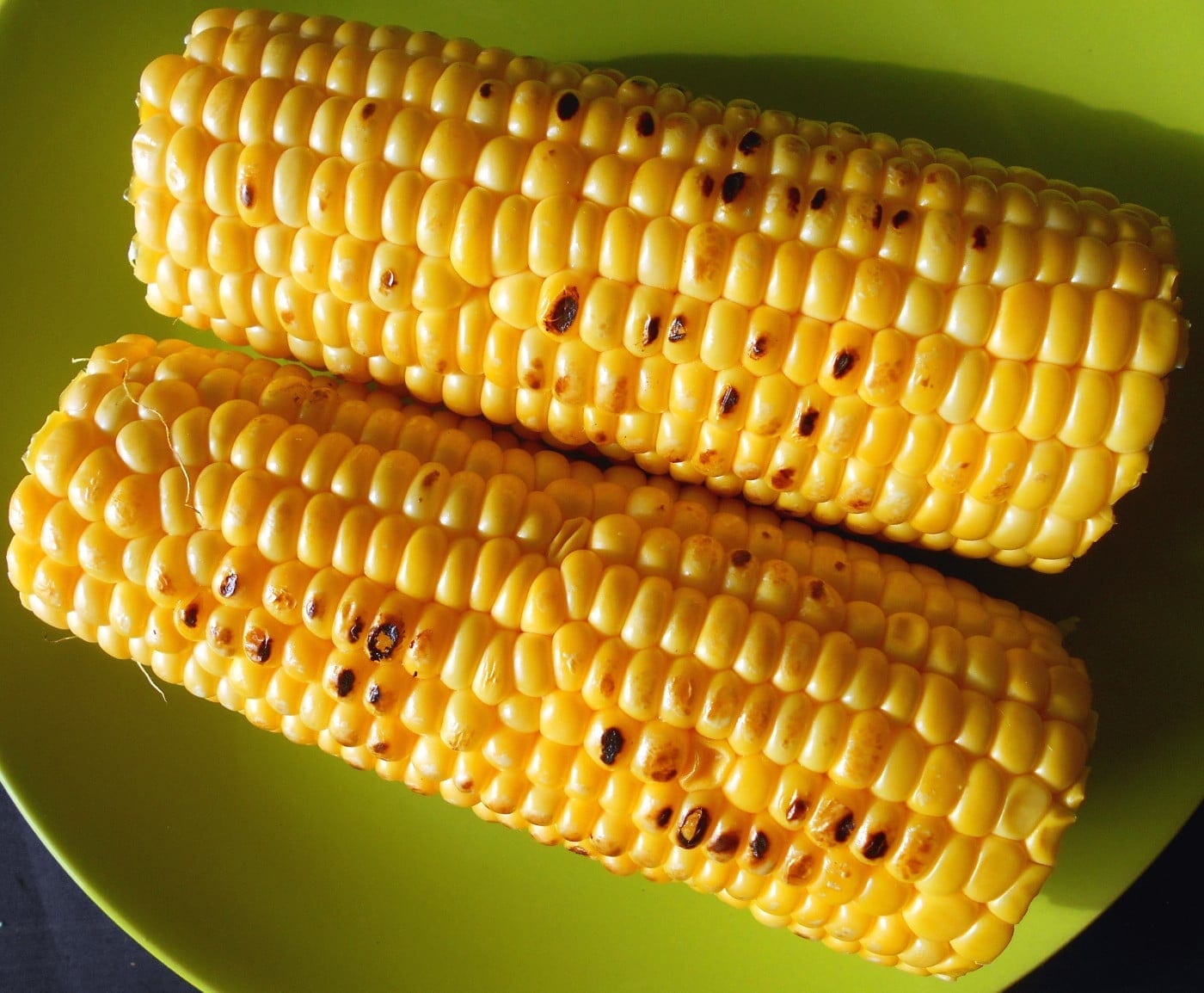 Two ears of grilled corn on a green plate.