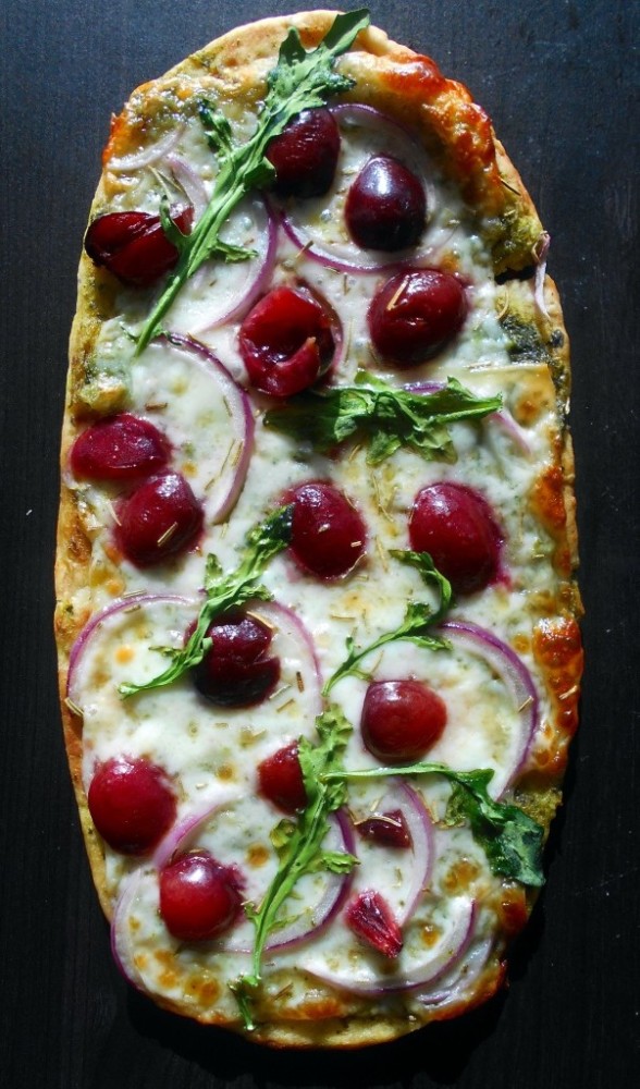 Overhead view of flatbread pizza topped with cheese and cherries 