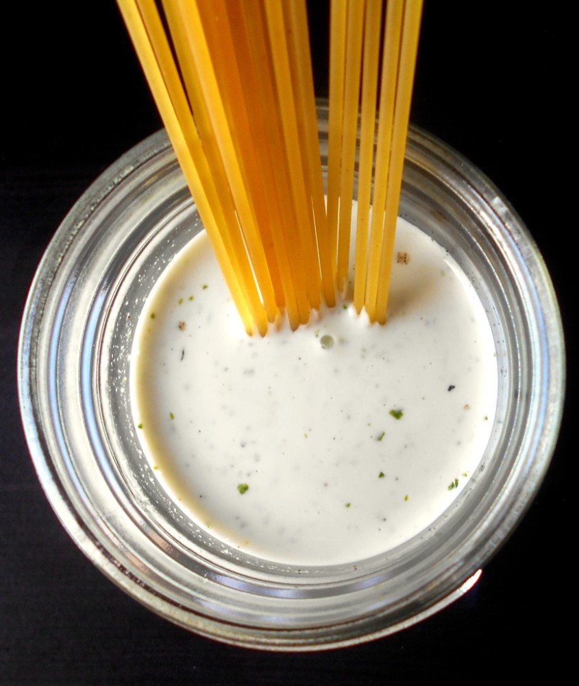 Overhead view of a mason jar filled with spicy lime dressing with spaghetti in it. 