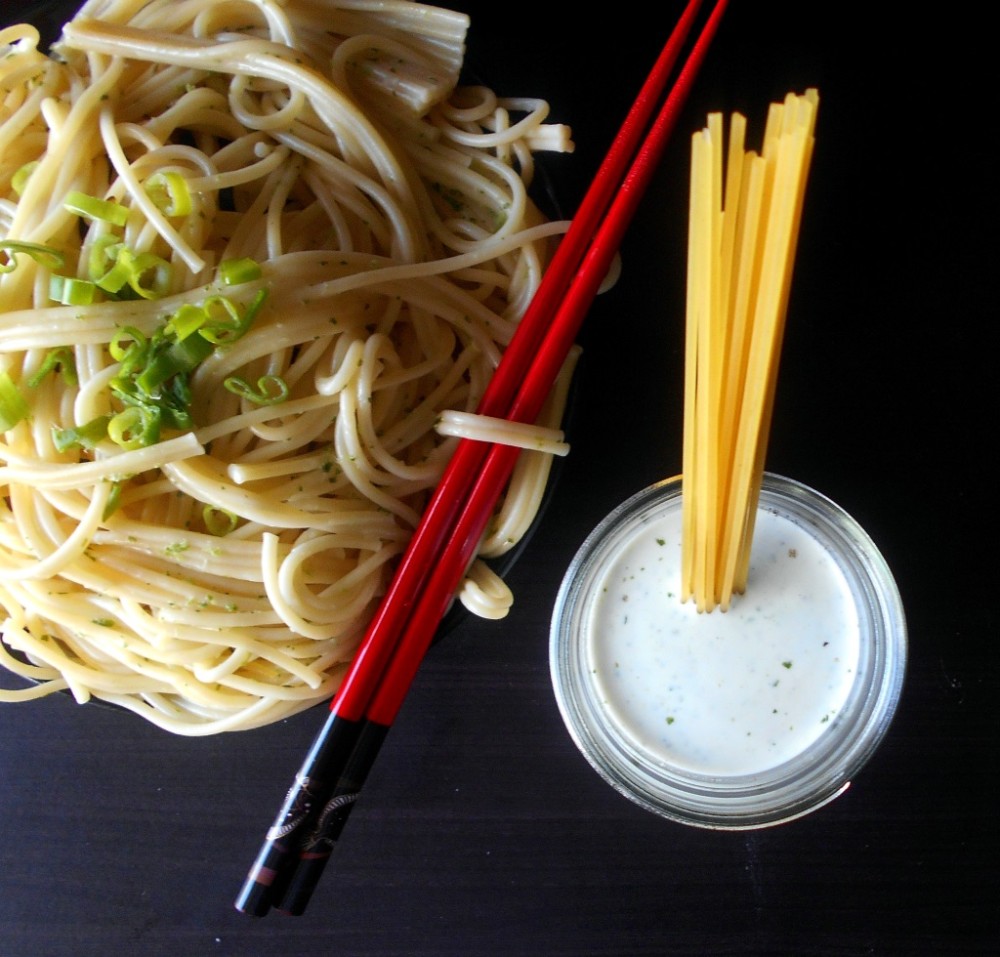 Overhead view of a mason jar filled with spicy lime dressing with spaghetti in it. In the back, a bowl of noodles is visible