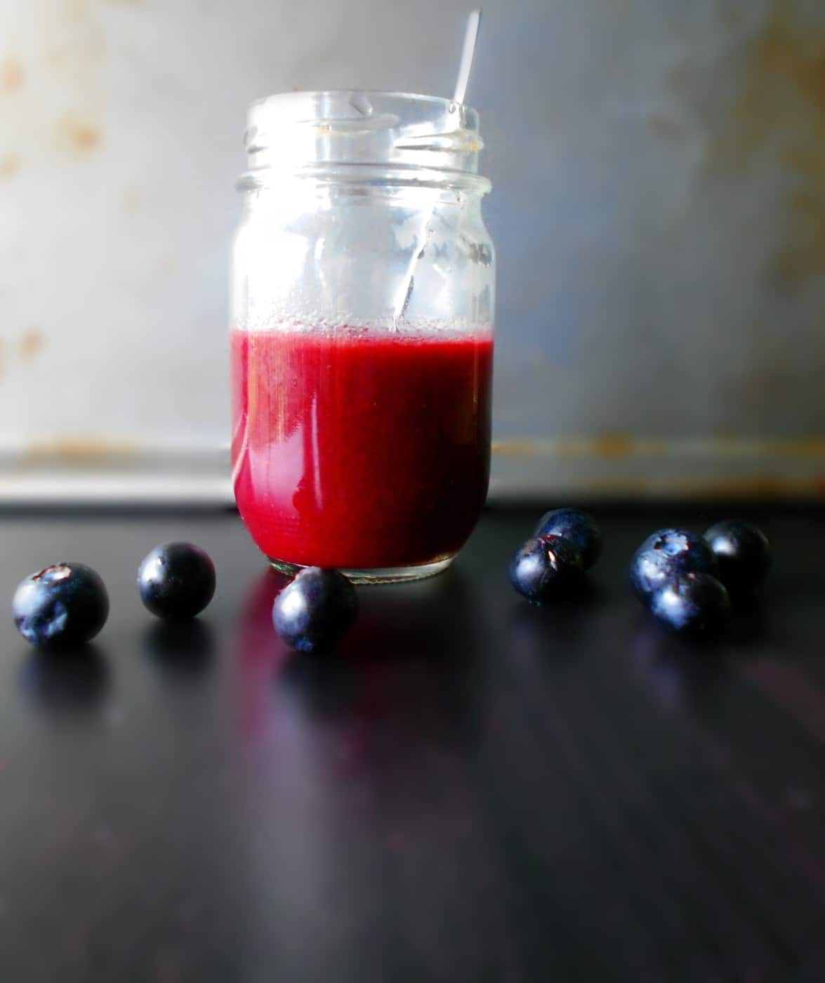 Front view of blueberry vinaigrette in a glass bottel with blueberry around
