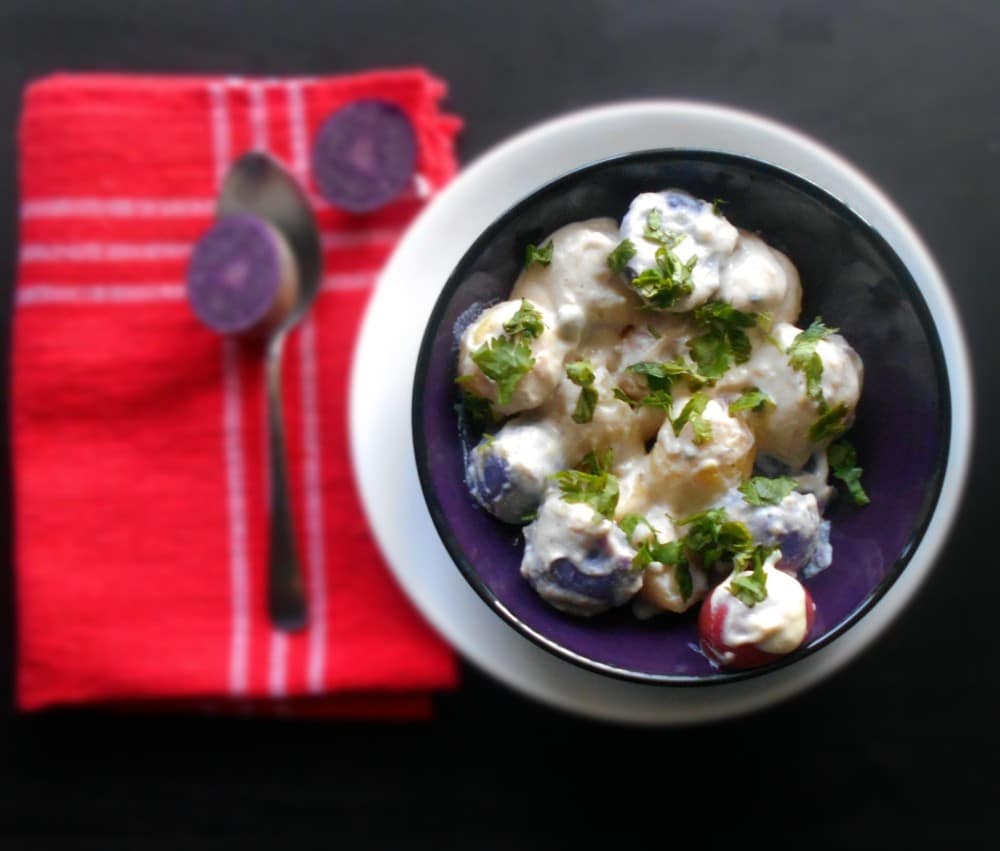 Top view of a dark blue bowl filled with multiple colors of potatoes in a white creamy liquid