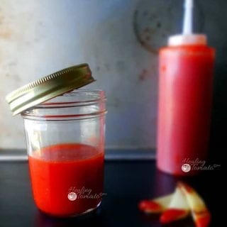 A mason jar with homemade ketchup recipe and a ketchup bottle in the background