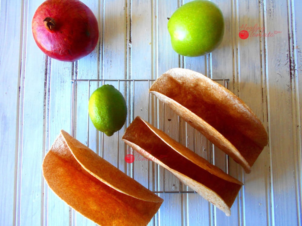 Overhead View of 3 Homemade Taco Shells Grande on a Cooling Rack with 1 Green Apple, 1 Lime and 1 Pomogranate Next to it