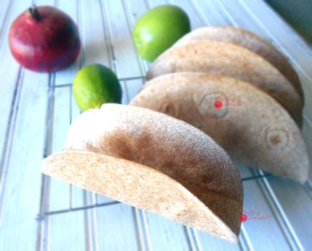 Top Angle View Homemade Taco Shells Grande on a Cooling Rack with 1 Green Apple, 1 Lime and 1 Pomegranate in the Background