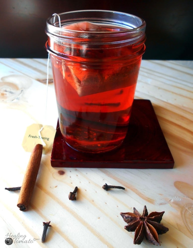 A tea bag inside a mason jar filled with hot toddy ingredients. Surrounded by cinnamon stick cloves and star anise