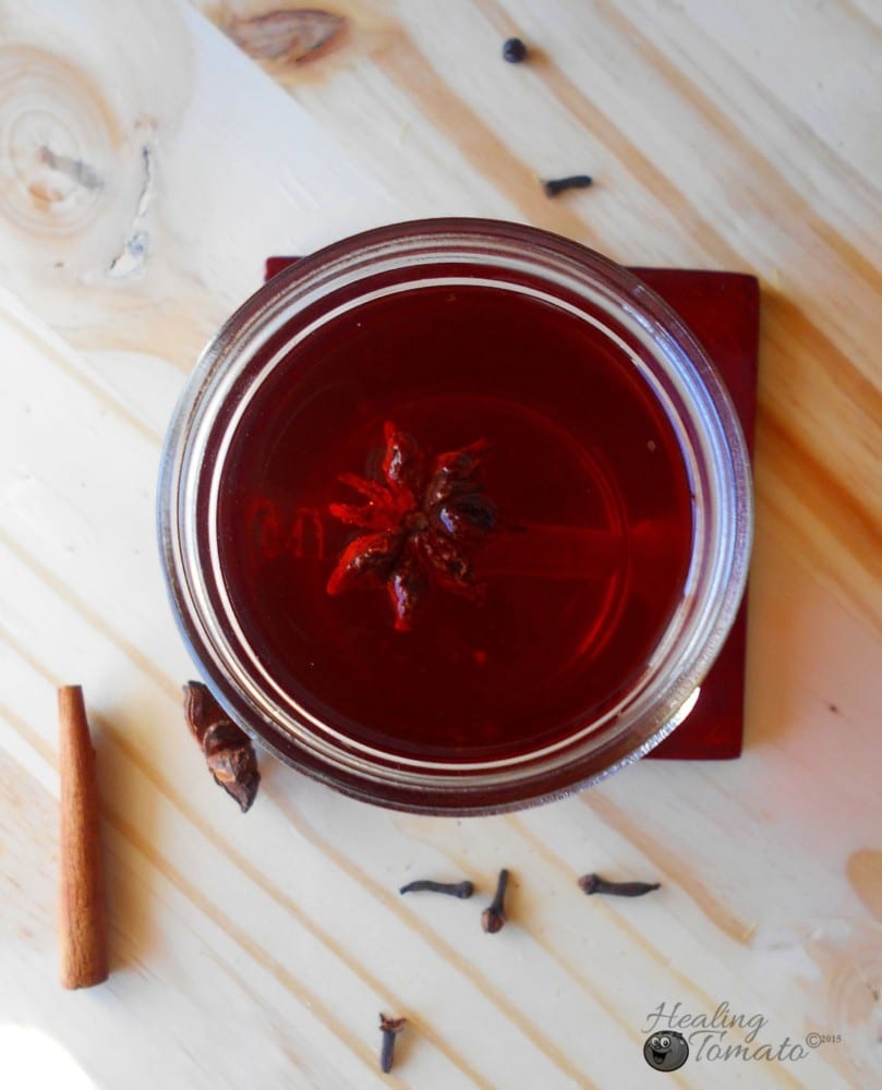 Closeup view of a tea bag inside a mason jar filled with hot toddy ingredients. Surrounded by cinnamon stick cloves and star anise