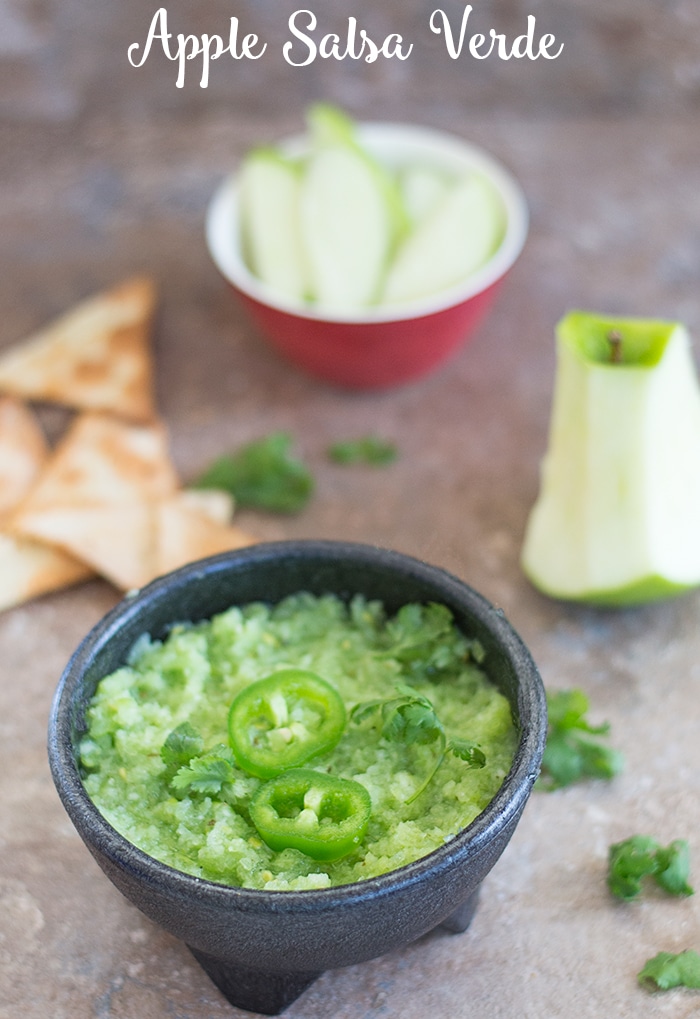 Angle view of a black mexican salsa bowl filled with apple salsa verde and surrounded by apples, cilantro and chips