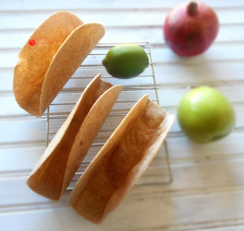 Overhead View Homemade Taco Shells Grande on a Cooling Rack with 1 Green Apple, 1 Lime and 1 Pomegranate on the Side