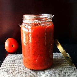 Front view of glass jar filled with a red sauce.