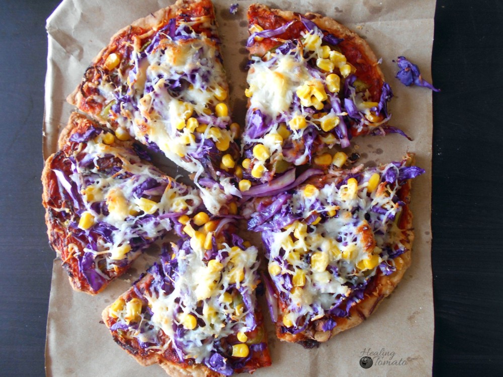 Overhead view of red cabbage pizza pie cut into slices. Corn and melted cheese visible