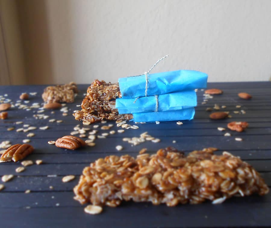 Front view of a homemade granola bar. More granola bars in the back with pecans and oatmeal scattred