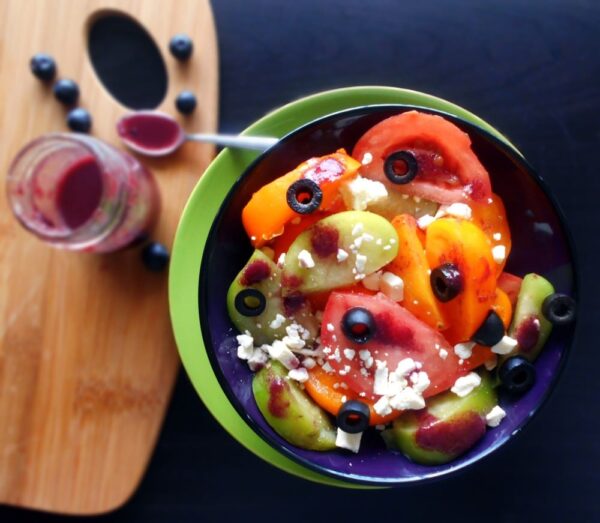 Top view of a mix of different tomatoes in a bowl with a bottle of blueberry sauce on the side. 