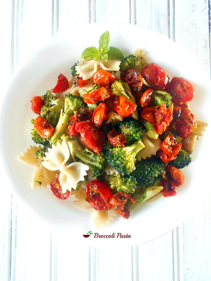 A white plate filled with roasted cherry tomatoes, broccoli and bow tie pasta