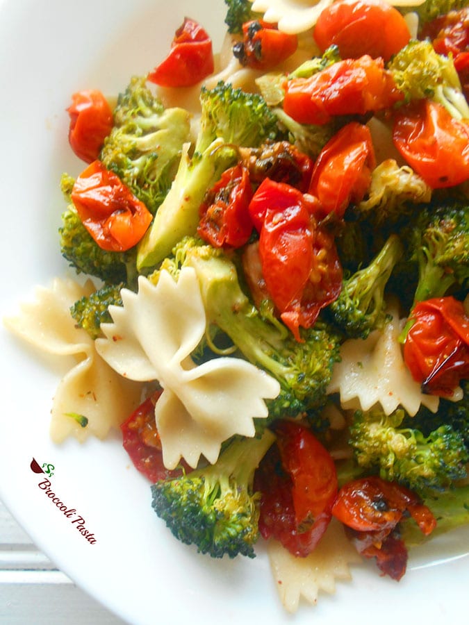 Closeup view of a white plate filled with roasted cherry tomatoes, broccoli and bow tie pasta