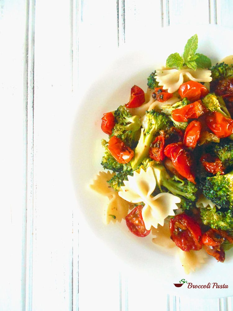 A white plate filled with roasted cherry tomatoes, broccoli and bow tie pasta