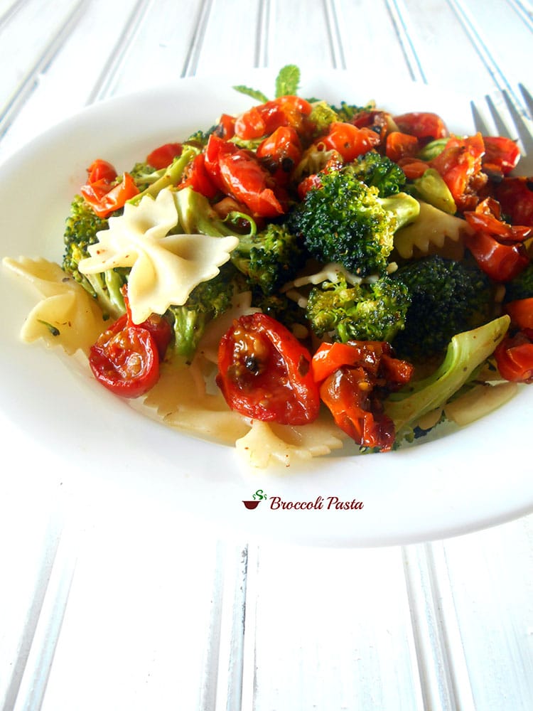 Front view of a white plate filled with roasted cherry tomatoes, broccoli and bow tie pasta