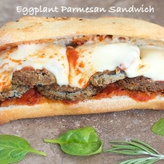 Front View of an Eggplant Sandwich with Melted Mozzarella Cheese and Surrounded by Spinach Leaves and Rosemary Sprigs