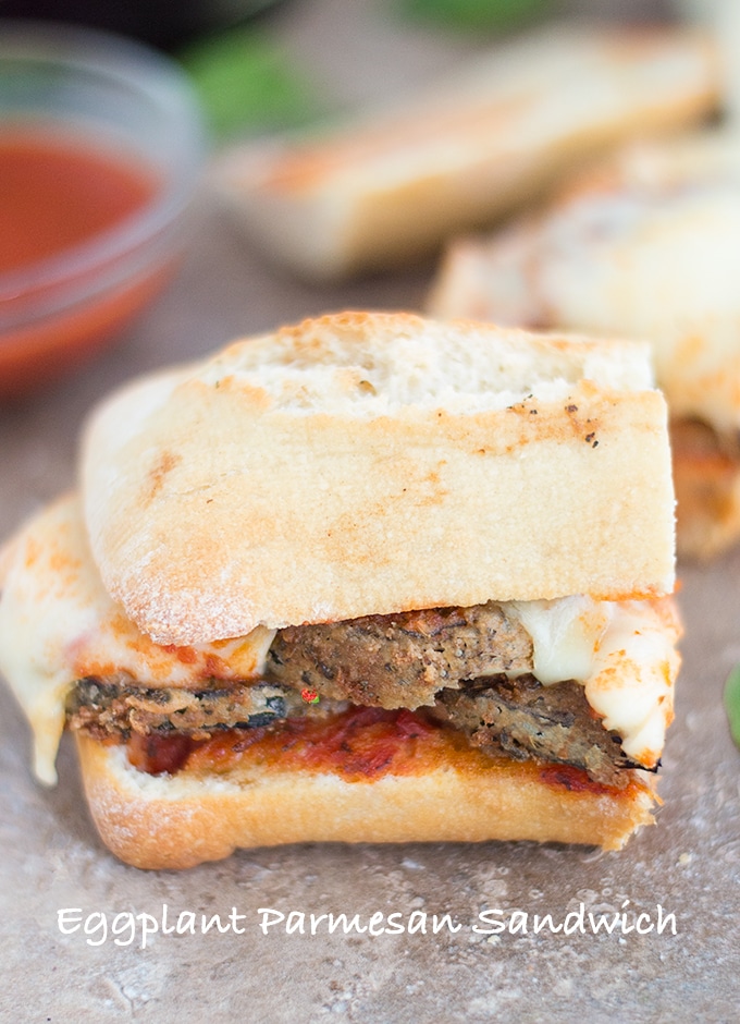 Front View of Half of an Eggplant Parmesan Sandwich with Melted Mozzarella Cheese and Surrounded by Spinach Leaves and Rosemary Sprigs