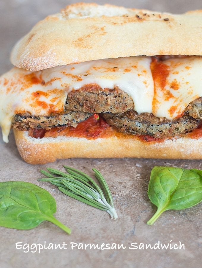 Front View of an Eggplant Sandwich with Melted Mozzarella Cheese and Surrounded by Spinach Leaves and Rosemary Sprigs
