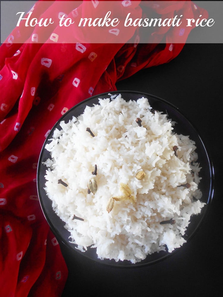 Overhead view of a black bowl filled with basmati rice and garnished with cloves, cardamom and ghee. A red sari / scarf is on the left