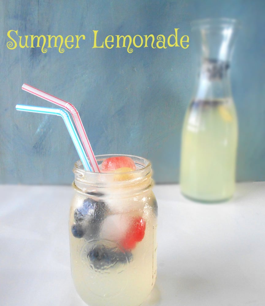 Front view of a glass with summer lemonade and fruit ice cubes. Long Pitches in the back filled with the same