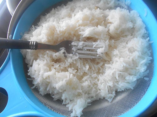 Top view of cooked rice in a nylon strainer with a fork on top