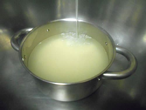 Water from tap going into a stainless steel pan filled with rice