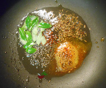 Overhead view of a pan with oil, mustard seeds and cumin seeds in oil and in a pan