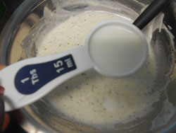 1 Tbsp measuring spoon with almond milk hovering over the yogurt - Saffron Yogurt Mayo