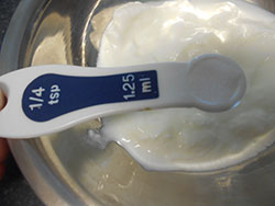 1/4 tsp measuring spoon with salt hovering over the yogurt - Saffron Yogurt Mayo