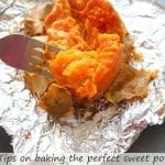 In the foreground, a fork with part of the pulp of the baked sweet potato. In the background, a baked sweet potato slit longitudinally and some of the skin peeled away to reveal the baked pulp