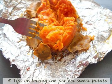 In the foreground, a fork with part of the pulp of the baked sweet potato. In the background, a baked sweet potato slit longitudinally and some of the skin peeled away to reveal the baked pulp