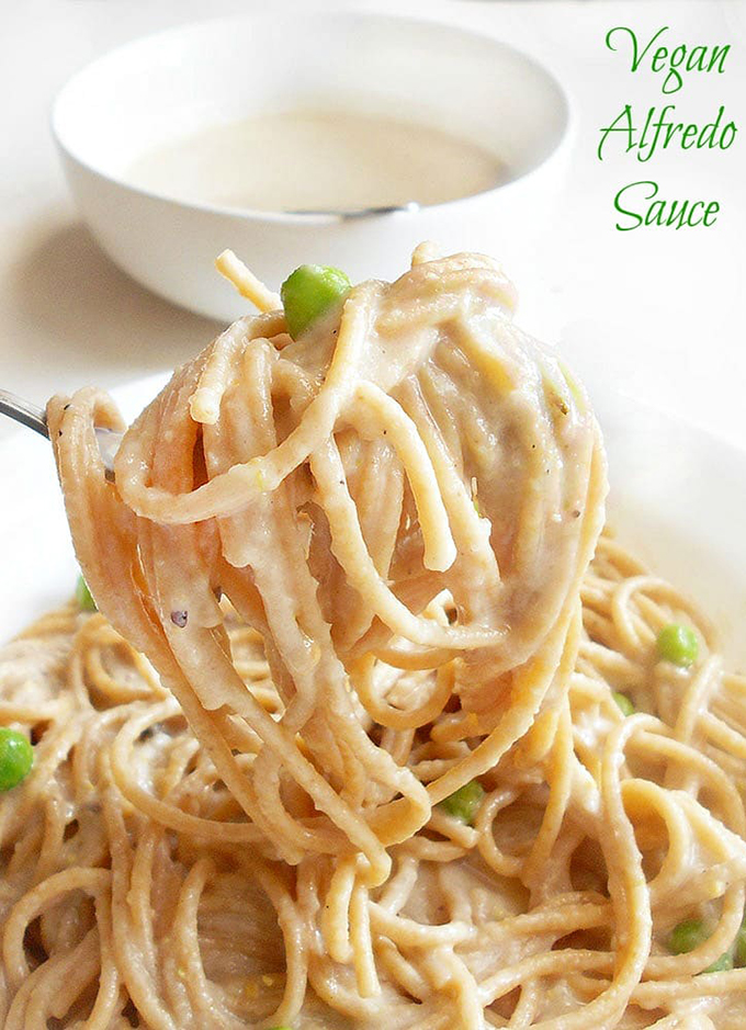 Closeup View of A Fork Lifting a Spaghetti with Alfredo Sauce. In the Background, There is a White Bowl Filled with th Alfredo Sauce and a Stainless Spoon In it