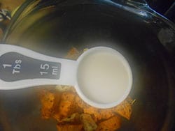 Overhead view of 1 Tbsp Measuring Spoon Filled with Almond Milk and Floating Over Sweet Potatoes in a Blender