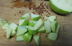 1/2 of a Green Apple Cubed on a Chopping Block. The Other Half of the Green Apple Partly Visible in the Background