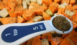 1 Tbsp measuring spoon filled with dried basil hovering over cubed sweet potatoes and radishes