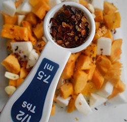 red pepper flakes in a 1/2 TBSP measuring spoon on top of a cubed veggetables 