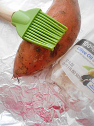 A sweet potato on placed on Foil and oiled. A green basting brush lies on top of the potato - 5 Tips on Baking The Perfect Sweet Potato